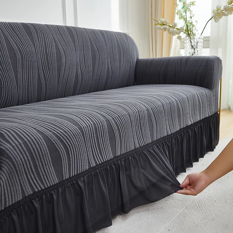 A dark gray jacquard stretch sofa cover with vertical stripes is draped over a sofa.