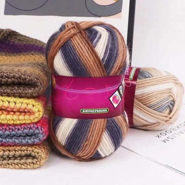 A ball of gradient dyed wool yarn in shades of brown, purple, and gray is shown next to a skein on a white background.
