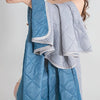 A folded blue and light gray quilted blanket draped over a person's shoulder.