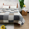 A gray and white checkered quilted bedspread is displayed on a bed with a white headboard and wooden nightstands.