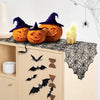 A Halloween display featuring carved pumpkins, a witch hat, and a black lace spider web table runner.