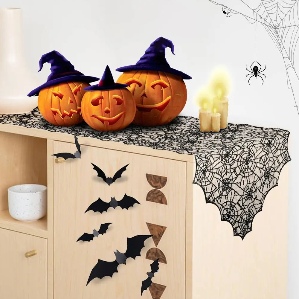 A Halloween display featuring carved pumpkins, a witch hat, and a black lace spider web table runner.