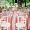 A round dining table set for an elegant event featuring pink satin tablecloths, white chairs, and floral centerpieces.