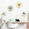 A collection of circular floral cross stitch embroidery designs displayed on a white wall above a wooden desk.