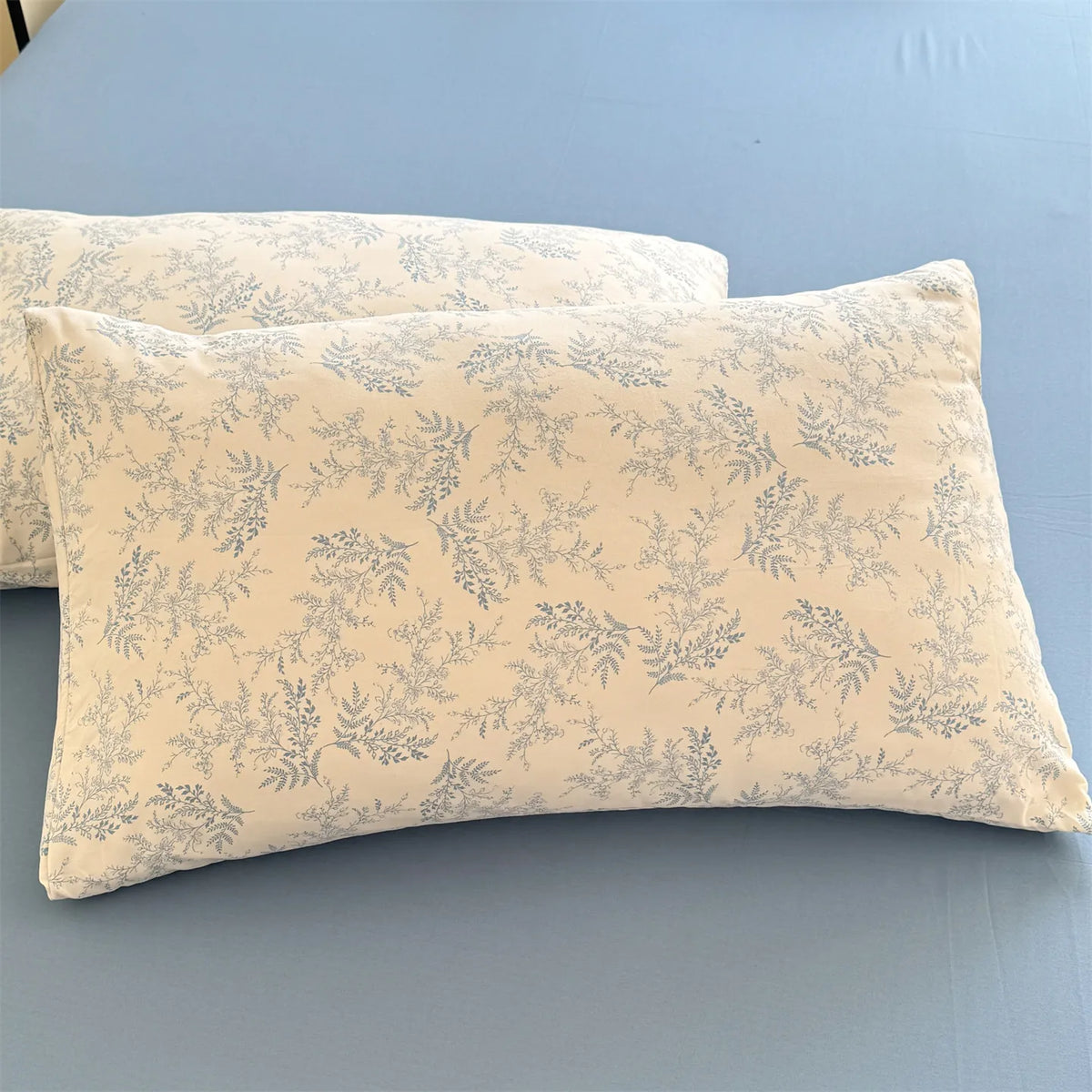 A light beige floral printed pillow cover resting on a blue surface.