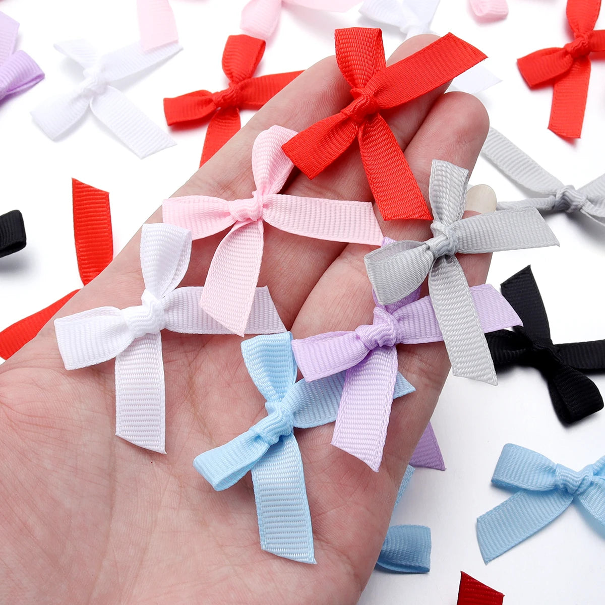 A hand holds various colored satin ribbon bows, including red, pink, white, and purple.