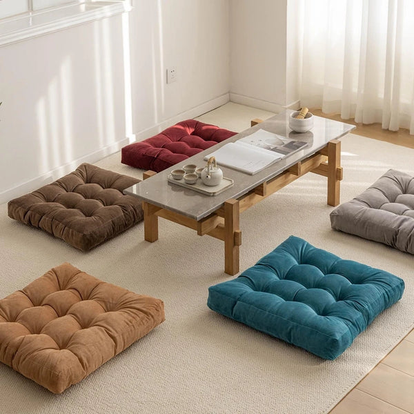 A collection of handmade tufted floor seat cushions in earthy tones and teal colors arranged on a light-colored rug.