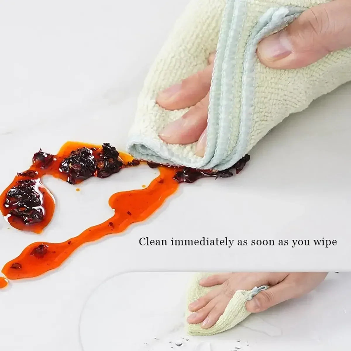 A hand wipes orange food stain from a white cloth, demonstrating the clear heat-resistant PVC tablecloth protector.