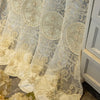 Ivory embroidered beaded sheer curtain with punched-hole design hanging next to a white cabinet.
