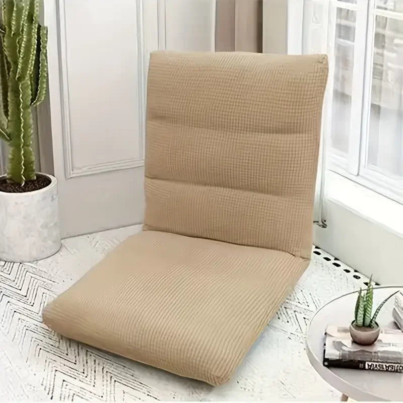 A beige folding tatami seat cover placed on a white floor, next to a potted plant and a window.