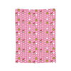 A pink patterned throw blanket featuring small embroidered characters and green accents.