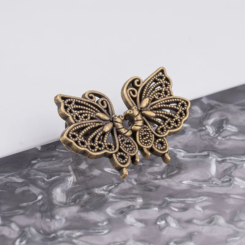 A vintage brass butterfly button waist tightener for pants and skirts resting on a gray textured surface.