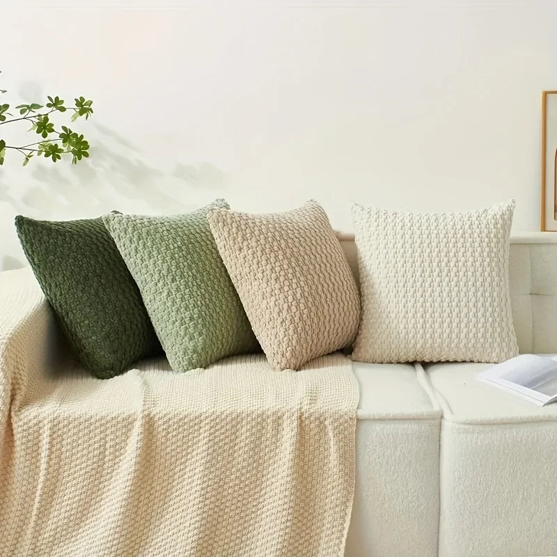 A collection of textured decorative pillow covers in shades of sage green and cream resting on a light-colored sofa.