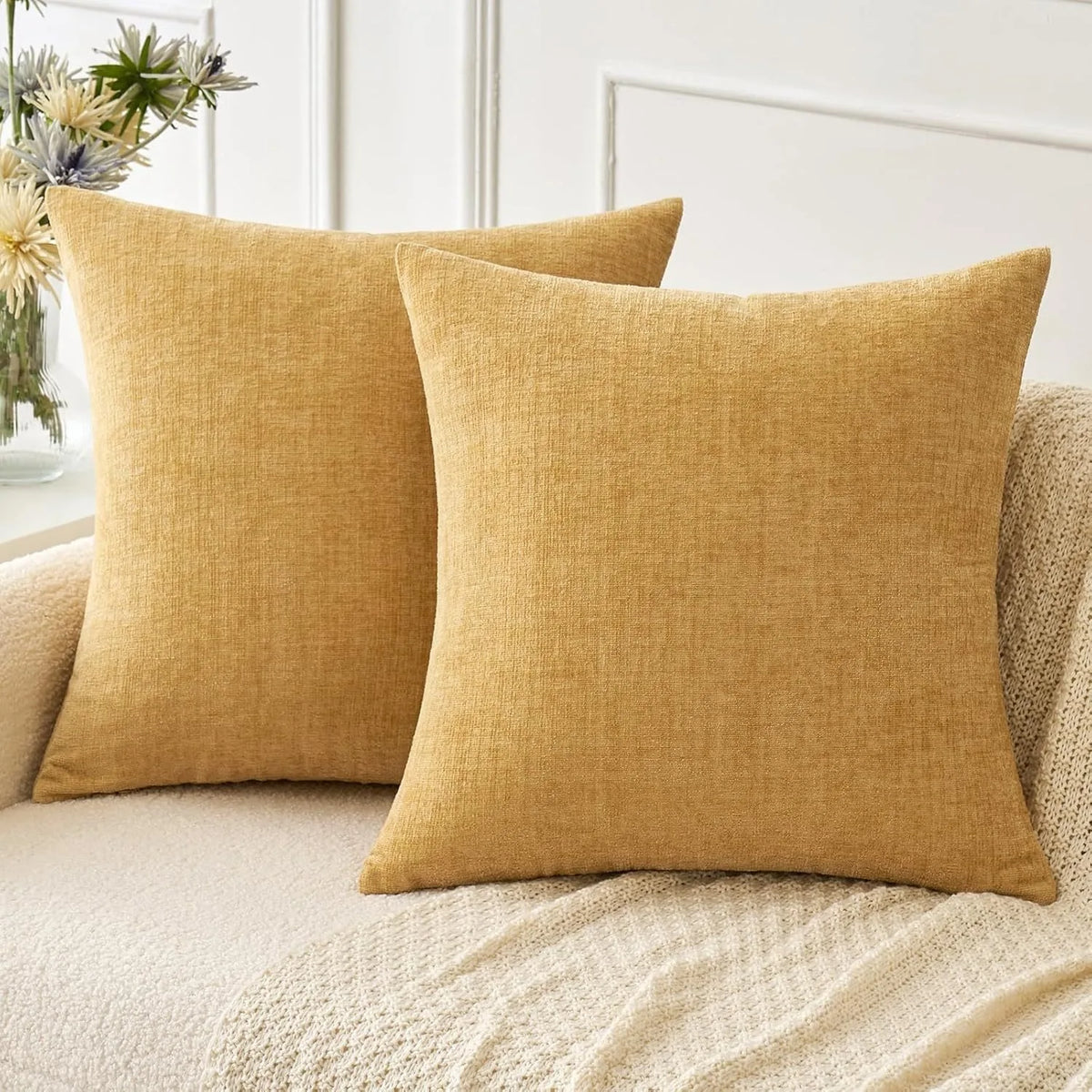 Two mustard yellow chenille throw pillows resting on a light beige sofa.