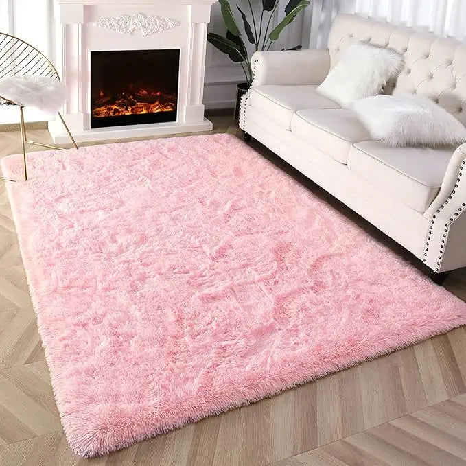 A fluffy pink tie-dyed plush floor mat placed in front of a white sofa and fireplace.