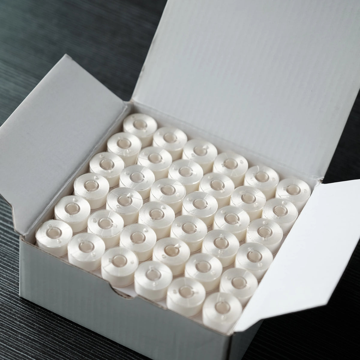 A white box filled with 144 rolls of high-quality polyester embroidery bobbin thread.