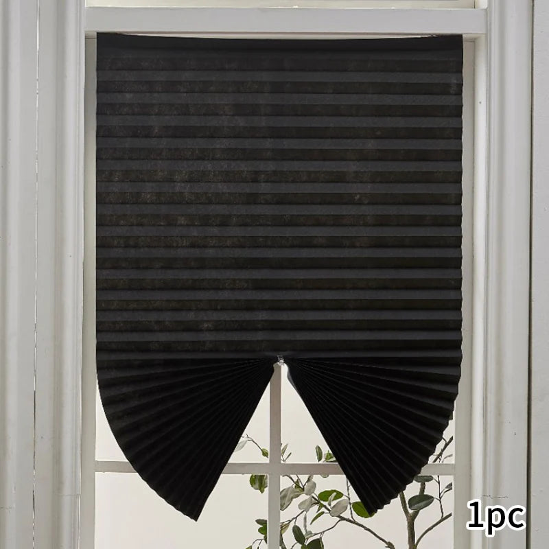 Black non-woven pleated blackout curtains hanging in a white window frame.