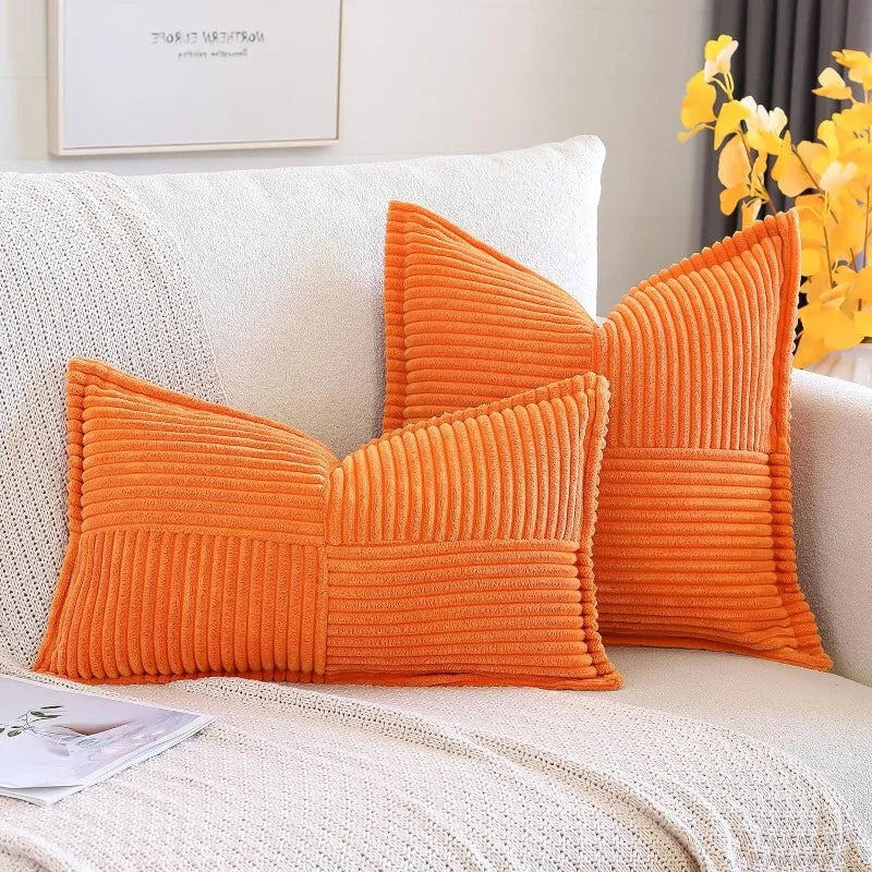 An orange striped corduroy lumbar support pillow cushion resting on a white sofa.