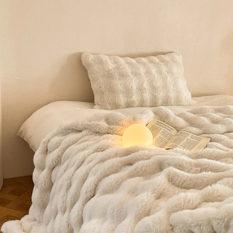 A fluffy white faux fur throw blanket draped over a bed, with an illuminated book resting on top.