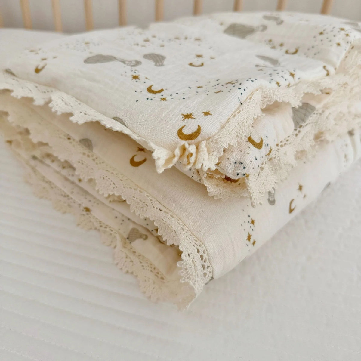 A folded cream muslin blanket with a floral print and gold star embroidery resting on a white surface.