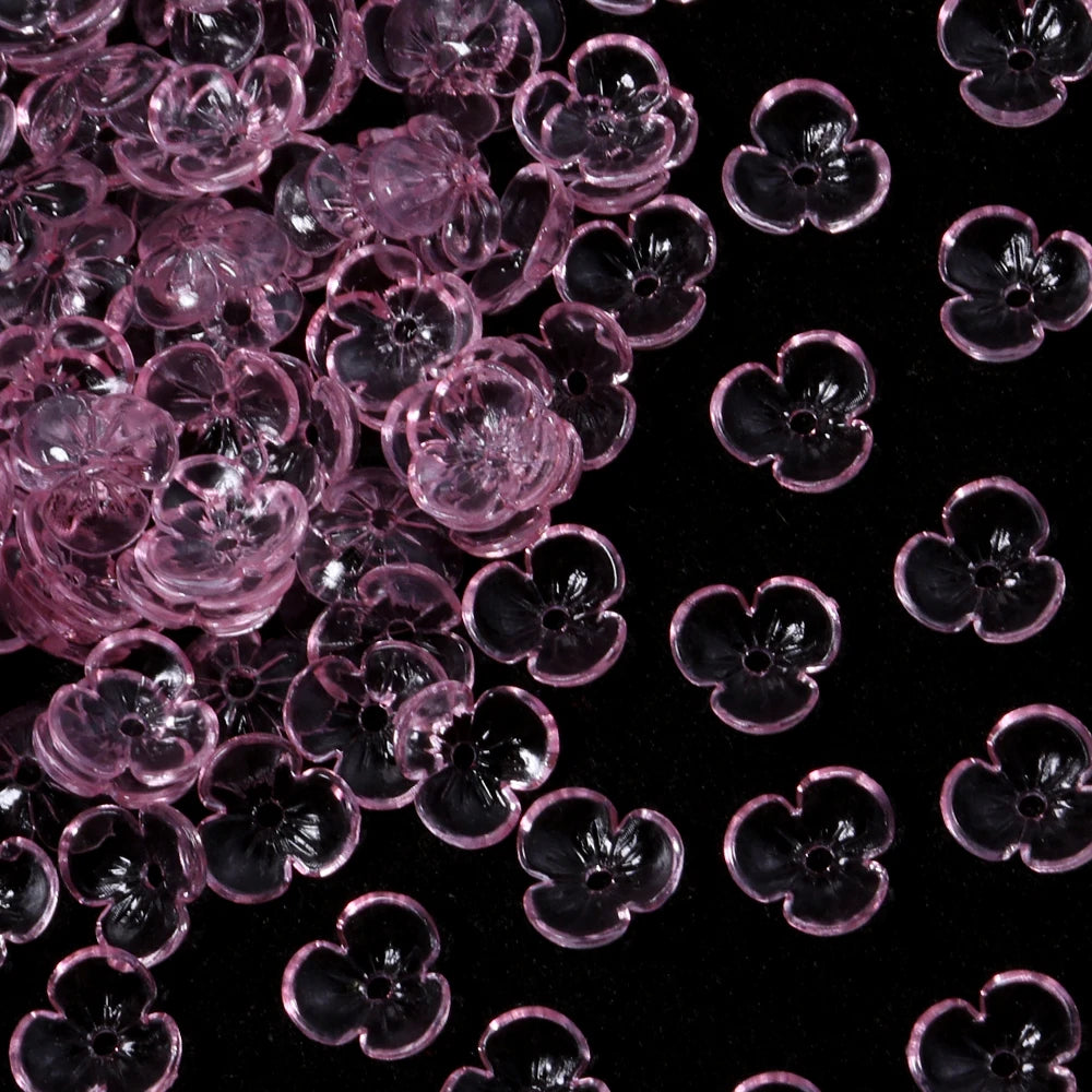 Close-up view of pink resin flower bead caps for jewelry making scattered on a dark background.