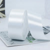 Rolls of white satin craft ribbons displayed on a sheet of paper.