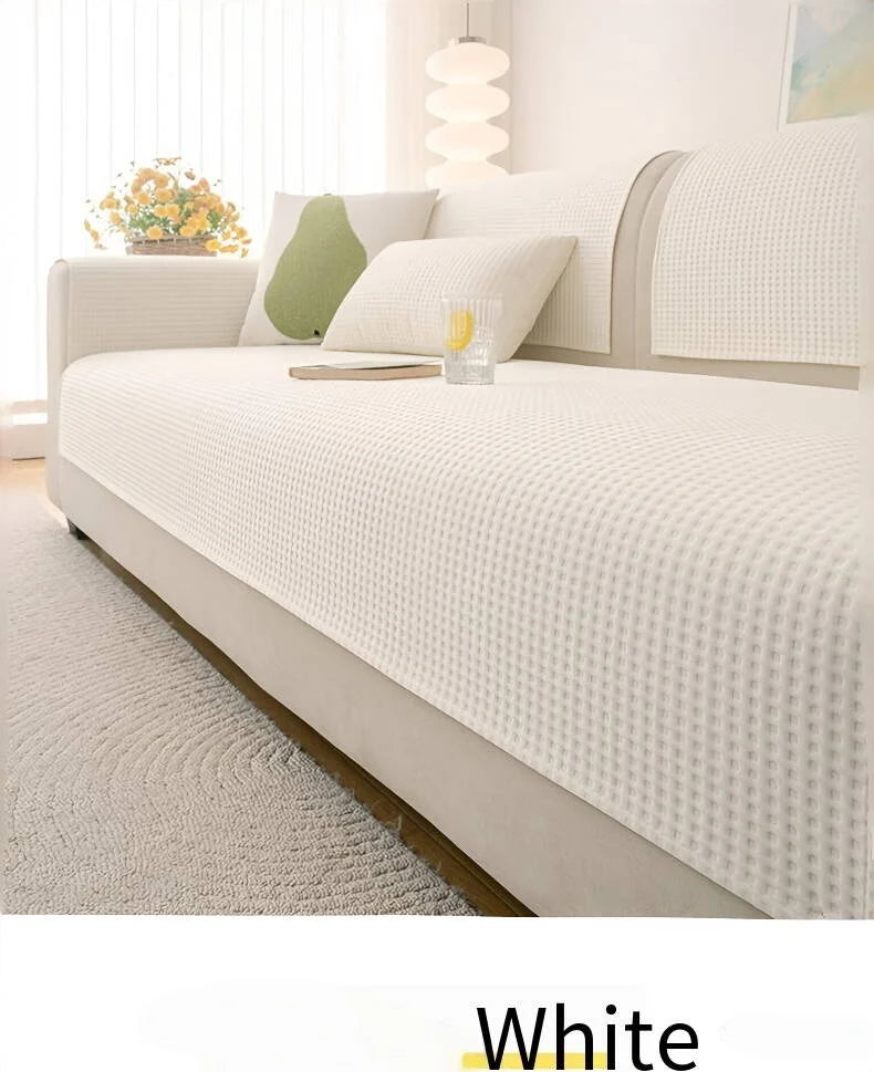 A white machine washable anti-slip sofa slipcover displayed on a bed with light bedding and natural light.