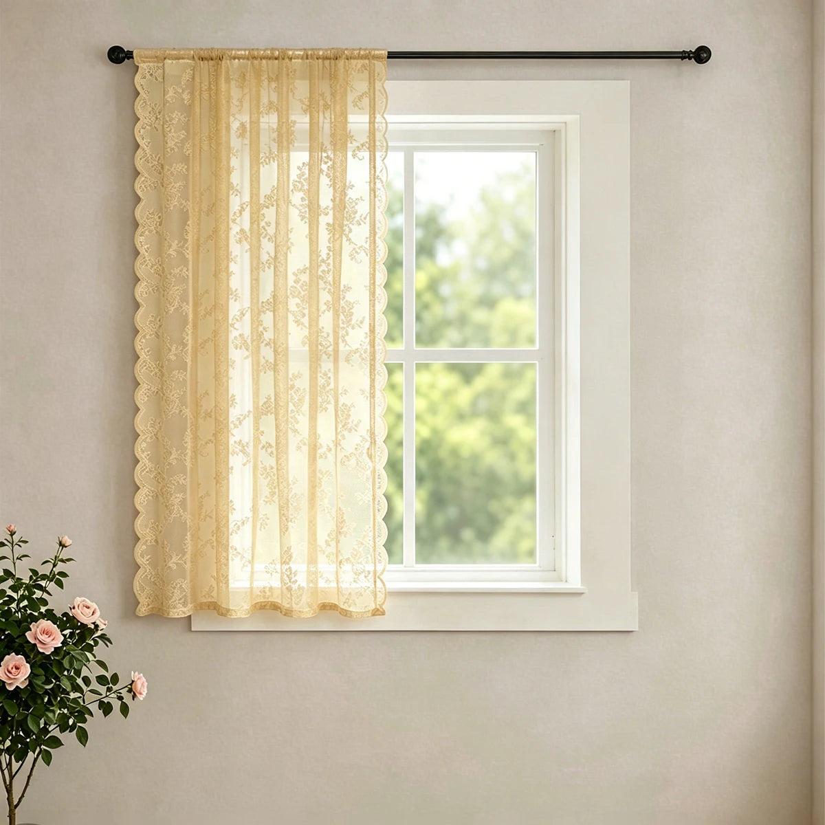 A sheer, cream-colored lace curtain with a wavy border hanging in a white window frame.