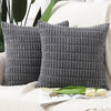 A set of two dark gray, textured knit throw pillow covers resting on a white knitted surface.
