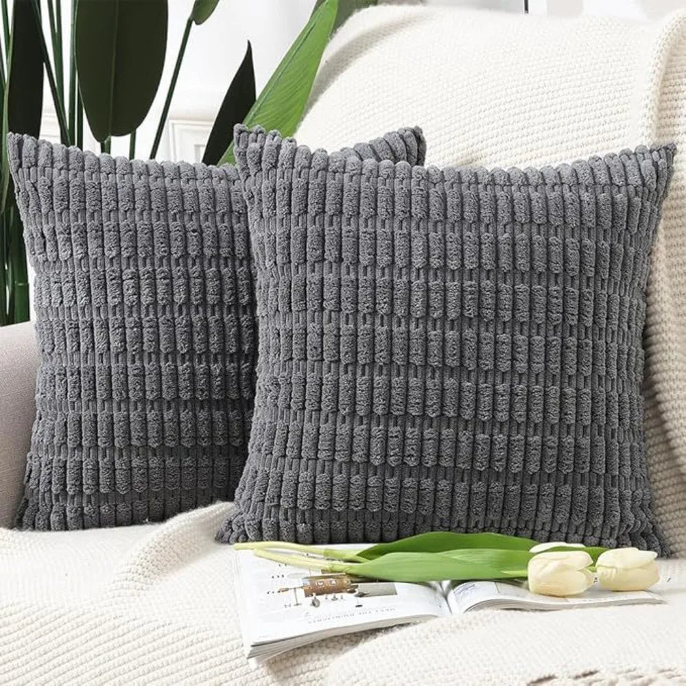 A set of two dark gray, textured knit throw pillow covers resting on a white knitted surface.