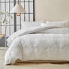 A white luxury quilt duvet set displayed on a bed with a light-colored wall and a modern pendant lamp.
