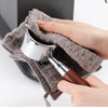 A hand is holding a metal cleaning tool inside a gray microfiber towel for coffee machines.