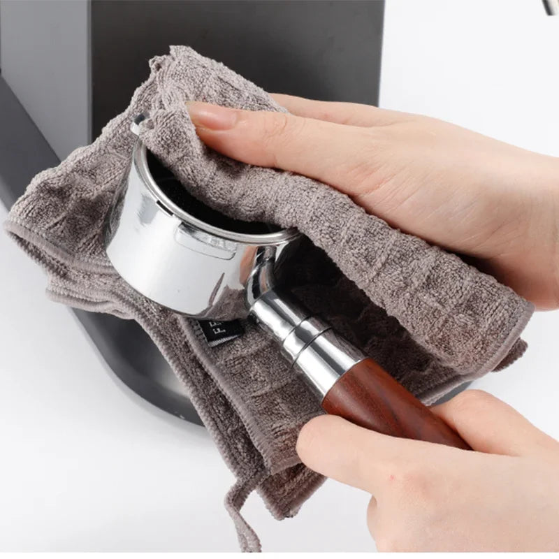 A hand is holding a metal cleaning tool inside a gray microfiber towel for coffee machines.