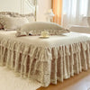 A bed dressed with a beige lace ruffled skirt and matching pillow covers in a bright bedroom setting.