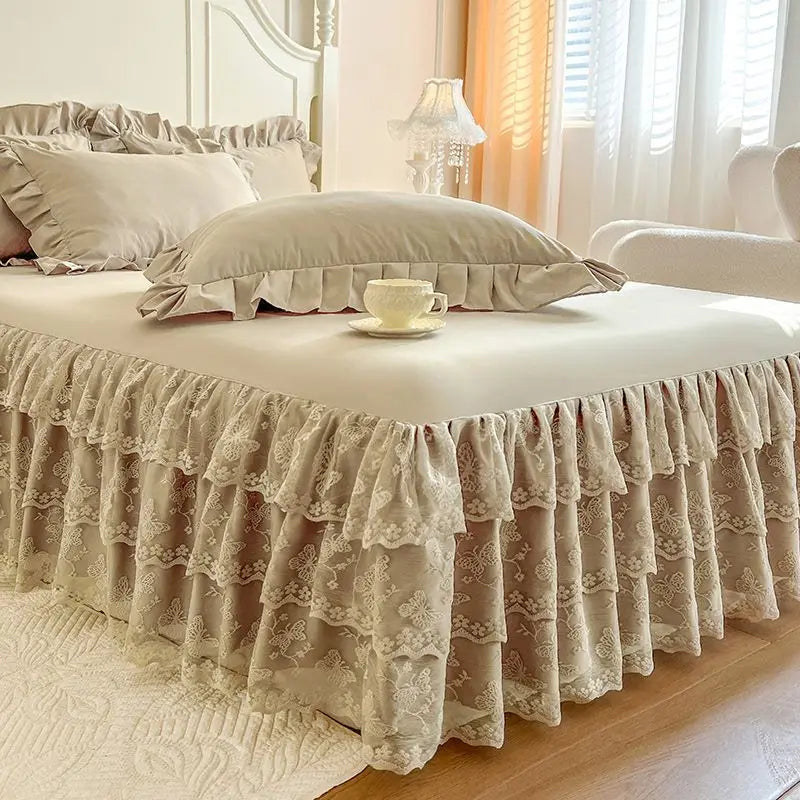 A bed dressed with a beige lace ruffled skirt and matching pillow covers in a bright bedroom setting.