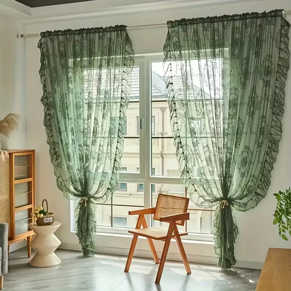 A pair of sheer green lace floral window curtains hanging in a light-filled room.