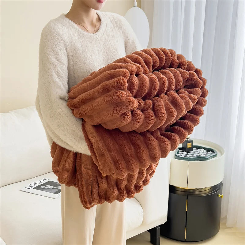 A person is holding a large, textured, brown plush blanket in front of a white sofa.