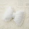 White elegant embroidered sofa cushion with lace trim resting on a white fluffy surface.