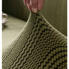 A hand is stretching a textured olive green fabric, demonstrating the elasticity of an elastic band.