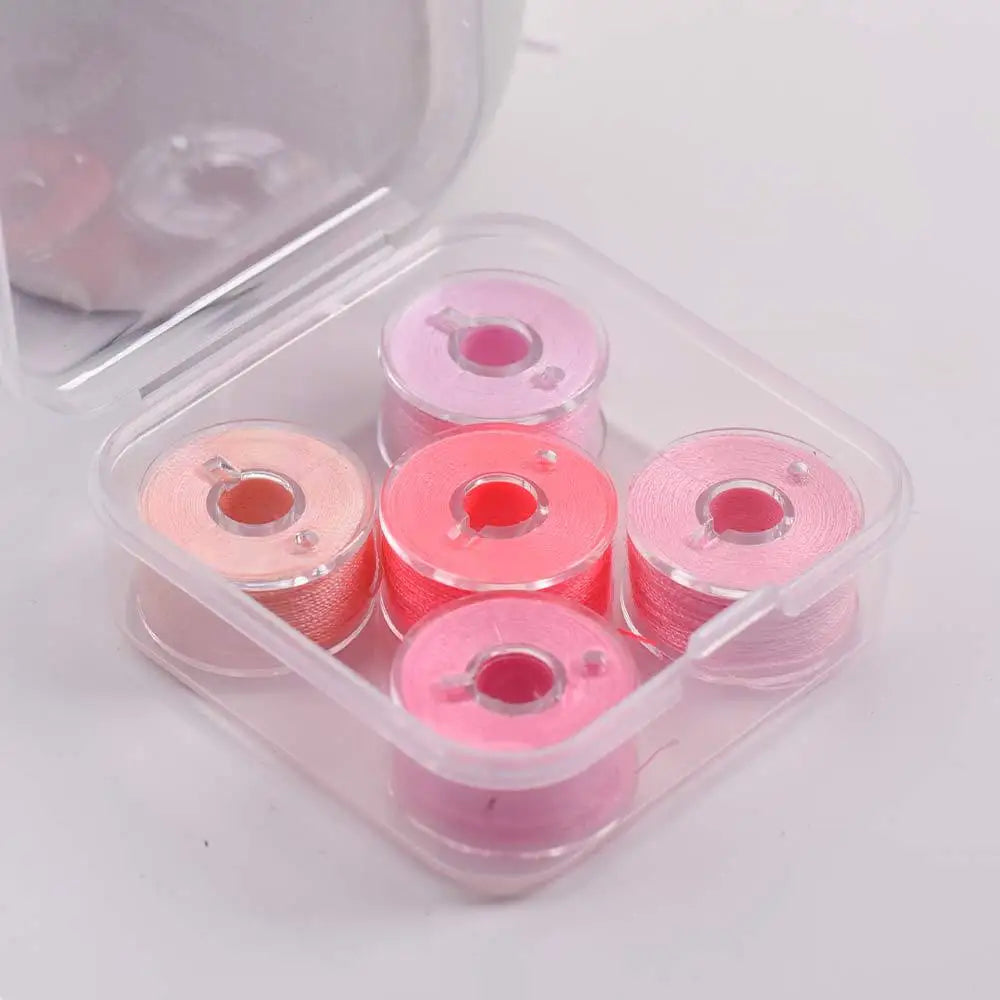 A clear plastic container holds various pink and magenta prewound sewing machine bobbin threads.