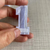 A hand holds a white, embroidered number patch shaped like the numeral one.