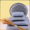 A stack of blue gray needle felting mats with a bundle of golden wheat stalks.
