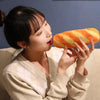 A woman is playfully biting into a loaf of orange bread, holding it with both hands.