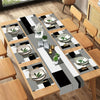A set of modern geometric placemats featuring black and white patterns with silver plates and small green plant accents.