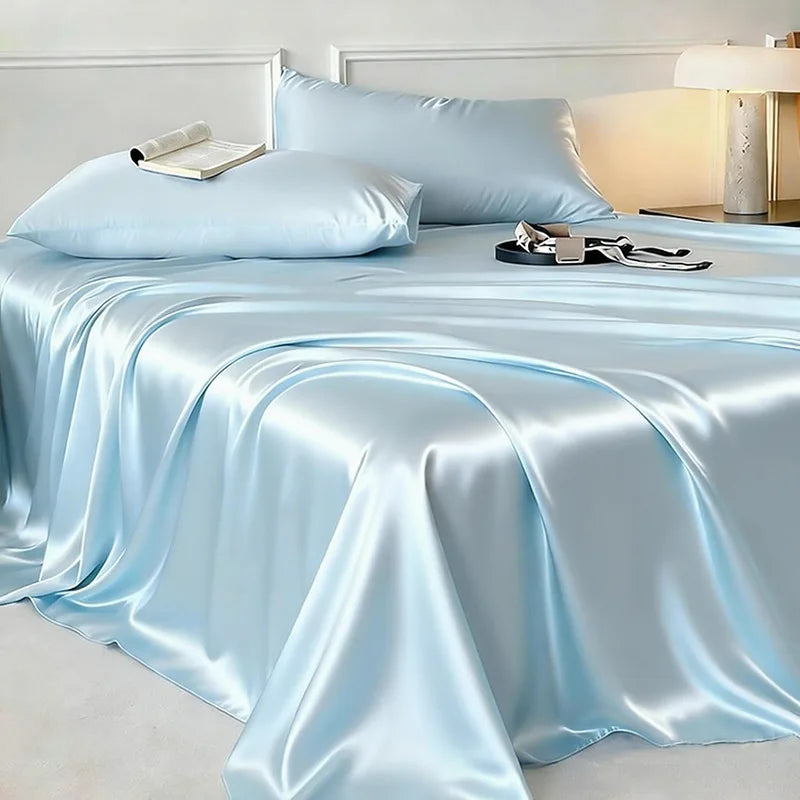 A silky light blue bed sheet draped over a bed with pillows and a bedside lamp.