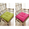 A woven rattan chair with a lime green and a pink tufted floor seat cushion.