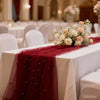 A deep red pearl beaded tulle table runner draped across a white tablecloth at an elegant event.
