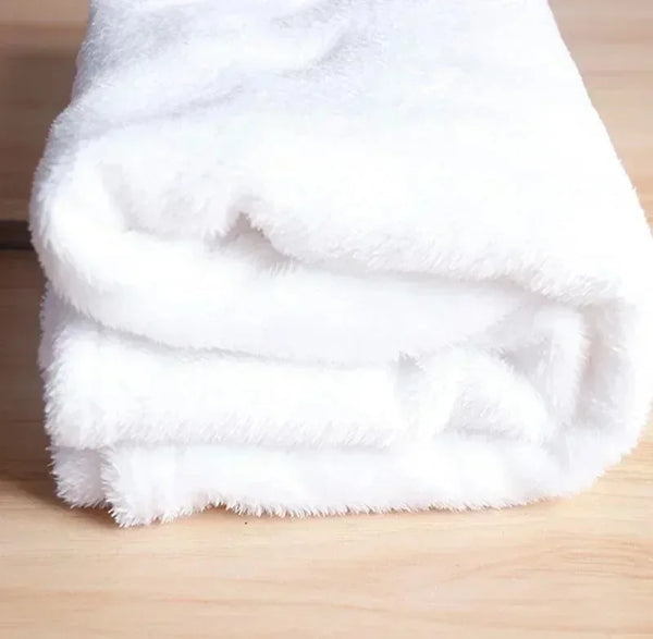 A stack of white, fluffy flannel throw blankets folded on a wooden surface.