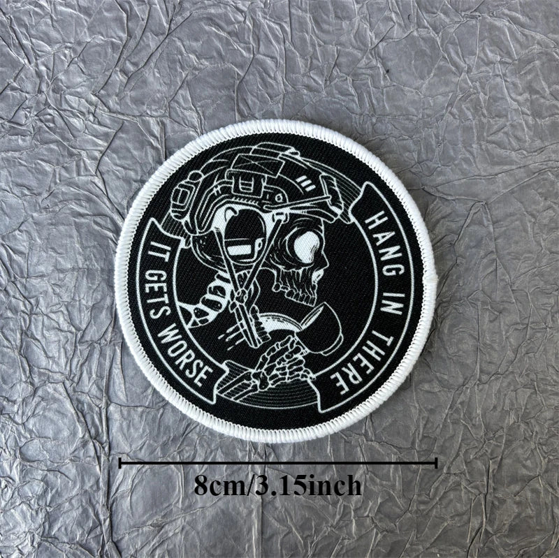 Black and white circular patch featuring a skull wearing a helmet with text that reads It Gets Worse Hang In There