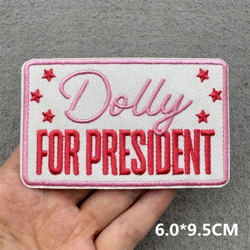 Pink embroidered patch with the text Dolly for President on a gray fabric background
